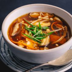 a white bowl filled with soup on top of a blue and white plate next to a spoon