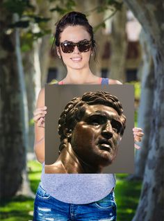 a woman holding up a photo of a bronze statue in front of trees and grass