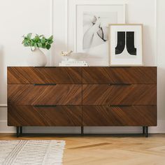 a wooden dresser sitting next to a white wall with pictures on it and a rug in front of it