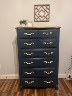 a blue dresser with gold handles in a room next to a white wall and wooden floor