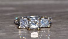 a three stone diamond ring sitting on top of a wooden table