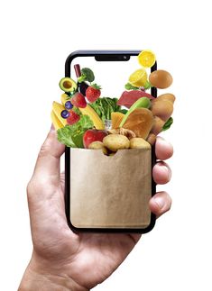 a hand holding a cell phone with a bag full of fruits and vegetables in it