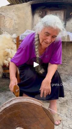 an old woman sitting on a chair next to a wooden barrel with wool in it