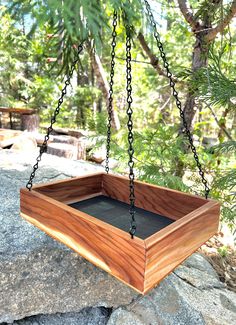 a wooden box hanging from a chain on top of a rock in front of some trees