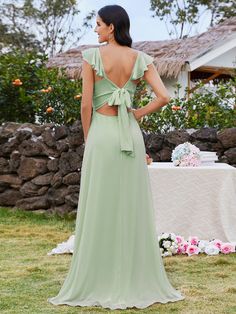 the back of a woman in a green dress standing on grass near a table with flowers