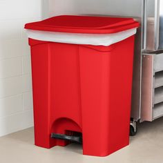 a large red trash can sitting next to a metal storage bin on the floor in front of a white tiled wall