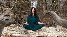 a woman sitting in the middle of a forest doing yoga