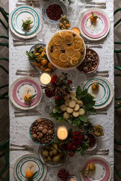 a table is set with plates and bowls filled with fruit, nuts, and vegetables