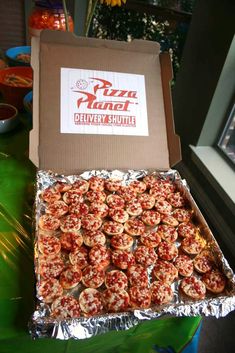 a box filled with mini pizzas sitting on top of a green table next to a window