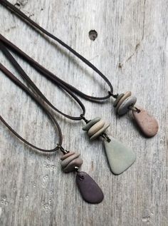 three necklaces with different shapes and colors on a wooden surface, one has a brown cord