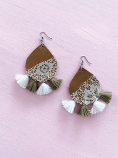 a pair of leather earrings with tassels and lace on the bottom, sitting on a pink background