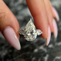 a woman's hand holding an engagement ring with two pear shaped diamonds on it