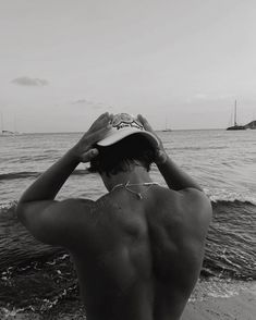 a man standing on top of a beach next to the ocean holding his hat over his head