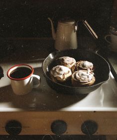 a pan filled with pastries on top of a stove next to a cup of coffee