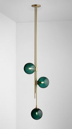 three green glass balls hang from a brass chandelier in a white walled room