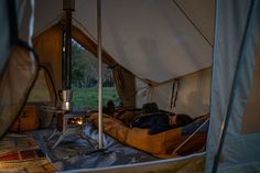 a man sleeping in a tent next to an open fire place with a lamp on it