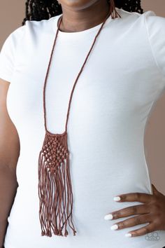 a woman wearing a white shirt with a brown necklace on her neck and hand in her pocket