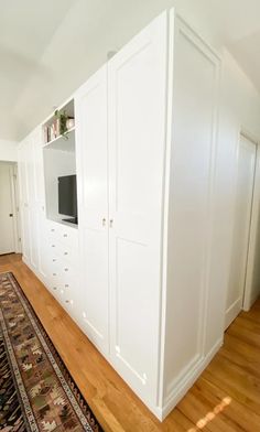 a room with white cabinets and a rug on the floor in front of an entertainment center