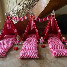 three beds with red and white striped sheets are set up in front of a stair case