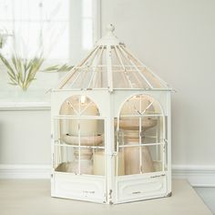 a white birdcage with two birds in it sitting on a table next to a window