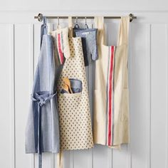 three aprons hanging on a rack with two wooden utensils in front of them