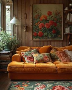 an orange couch in front of a window with flowers on the wall and rugs