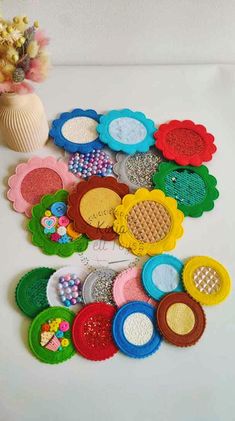 a bunch of different colored buttons sitting on top of a white table next to a vase with flowers