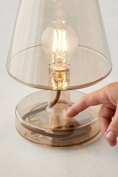 a person pointing at a light on a table with a glass shade over the lamp