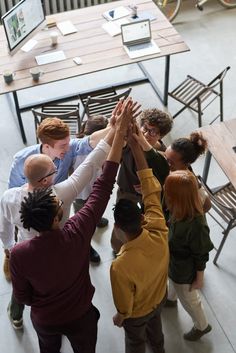 a group of people standing around each other with their hands in the air above them