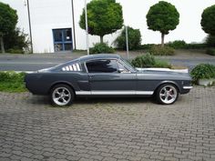 a gray mustang sitting on top of a cobblestone road