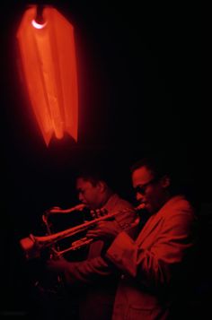 two men playing instruments in front of a bright red light with an object behind them