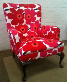 an upholstered chair with red and white flowers on the seat is sitting in front of a brick wall