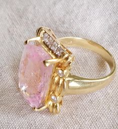 a fancy ring with a large pink stone surrounded by small white diamonds on a beige cloth