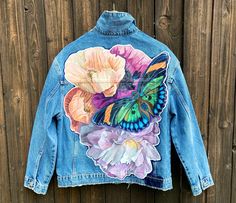 a blue jean jacket with an image of a butterfly and flowers painted on the back