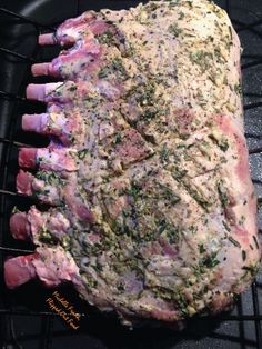 a large piece of meat sitting on top of a grill grate covered in herbs