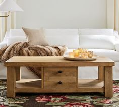 a coffee table with candles on it in front of a white couch and rugs