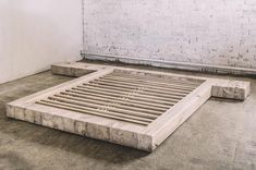 an unfinished bed frame sitting on the ground in front of a white brick wall and floor