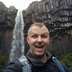 a man is taking a selfie in front of a waterfall with his backpack on