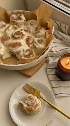 a white plate topped with cinnamon rolls next to a candle