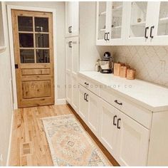 a kitchen with white cabinets and wood flooring next to a wooden door on the wall