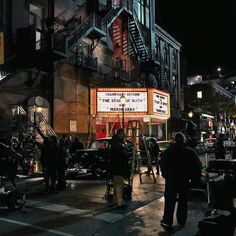 people standing on the street in front of a building with a movie marquee