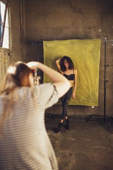 a woman taking a selfie in front of a yellow backdrop while another person takes a photo