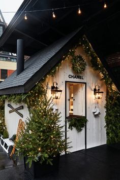 a small white building with christmas decorations on the outside and lights hanging from it's roof