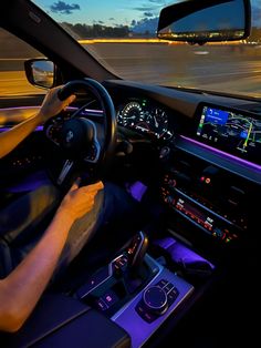 a man driving a car at night on the road with his hands on the steering wheel