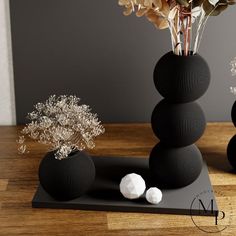 three black vases sitting on top of a wooden table next to flowers and plants