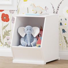 an elephant stuffed animal in a white cubby with flowers on the wall behind it