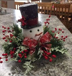 a snowman decoration on top of a table with red berries and holly wreaths