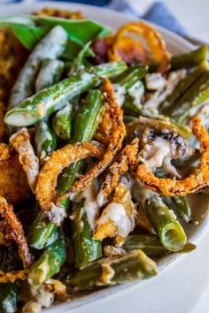 a white plate topped with green beans covered in cheese and onion rings on top of it