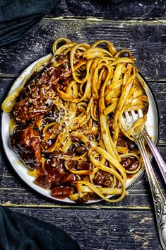 a plate of spaghetti with meat and sauce on it next to two silver spoons