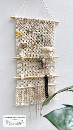 a macrame wall hanging with beads and other items attached to it, next to a potted plant